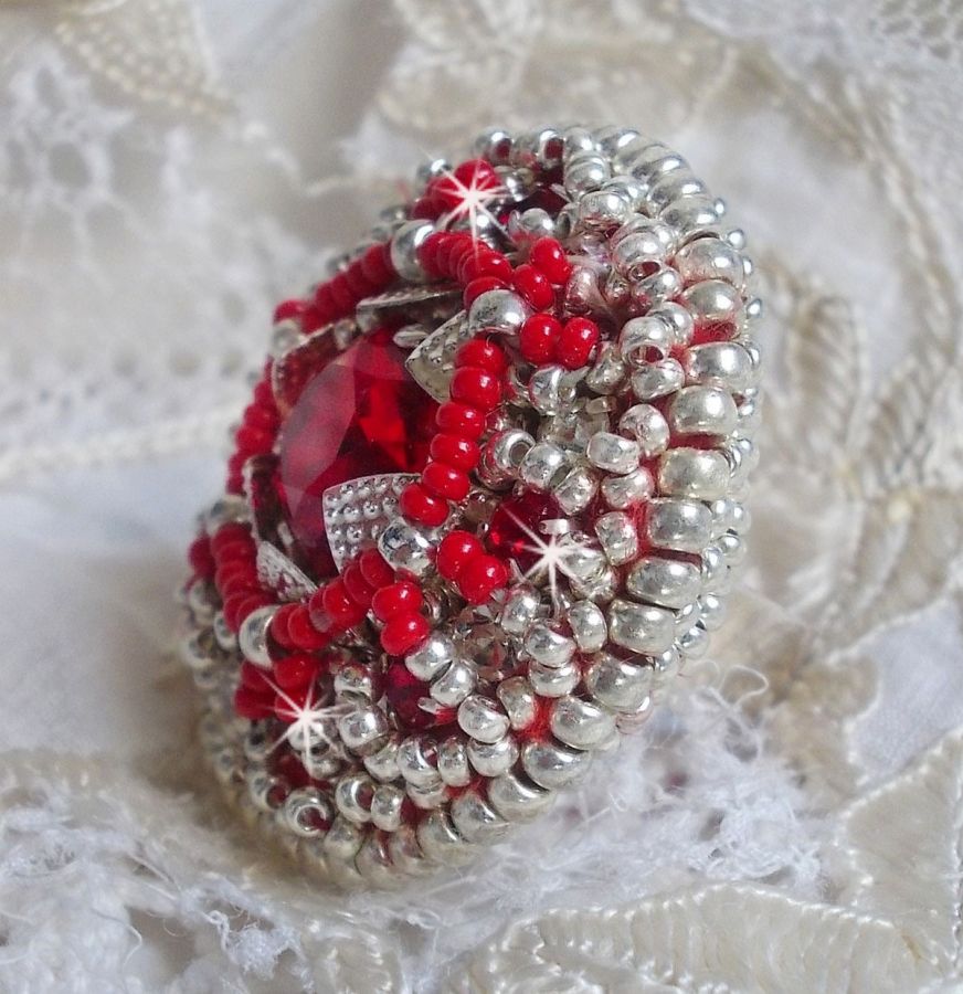 Bague Drigon Red brod&eacute;e avec un cabochon carr&eacute; Rouge sur une estampe Argent&eacute;e. Orn&eacute;e de chatons en Cristal puis model&eacute;e avec des rocailles et perles. Le tout est mont&eacute; sur une bague r&eacute;glable argent&eacute;e 
