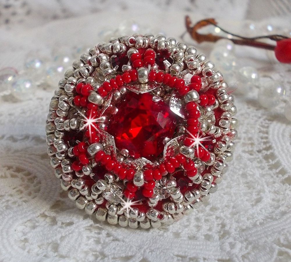 Bague Drigon Red brod&eacute;e avec un cabochon carr&eacute; Rouge sur une estampe Argent&eacute;e. Orn&eacute;e de chatons en Cristal puis model&eacute;e avec des rocailles et perles. Le tout est mont&eacute; sur une bague r&eacute;glable argent&eacute;e 