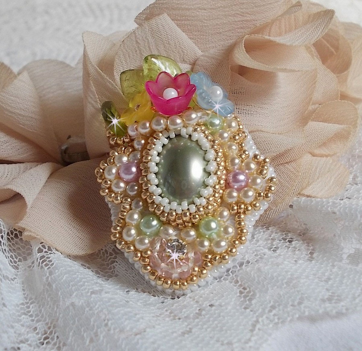 Bague Envol&eacute;e Fleurie brod&eacute;e avec un cabochon ovale Olivine en r&eacute;sine, orn&eacute;e de perles rondes nacr&eacute;es, des rocailles, fleurs Lucites, mini gouttes, chaton en Cristal et perles rondes aplaties.