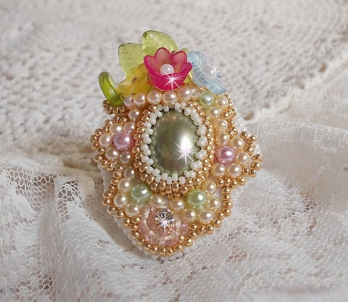 Bague Envol&eacute;e Fleurie brod&eacute;e avec un cabochon ovale Olivine en r&eacute;sine, orn&eacute;e de perles rondes nacr&eacute;es, des rocailles, fleurs Lucites, mini gouttes, chaton en Cristal et perles rondes aplaties.