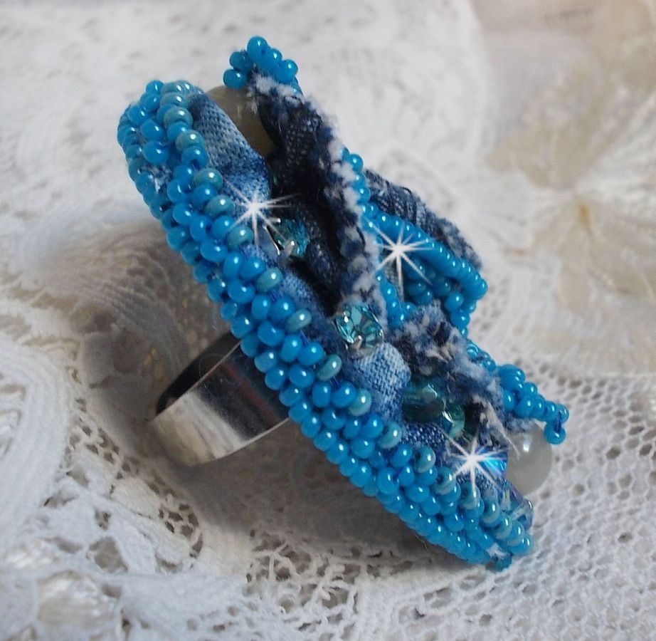 Bague Far West tout en jean brod&eacute;e avec des pierres de Gemme : Le Sodalite et le Jade Jaune &agrave; laquelle s'ajoute un tissu en Jean, un tissu mouchet&eacute; de fleurs avec des chatons en Cristal et des toupies