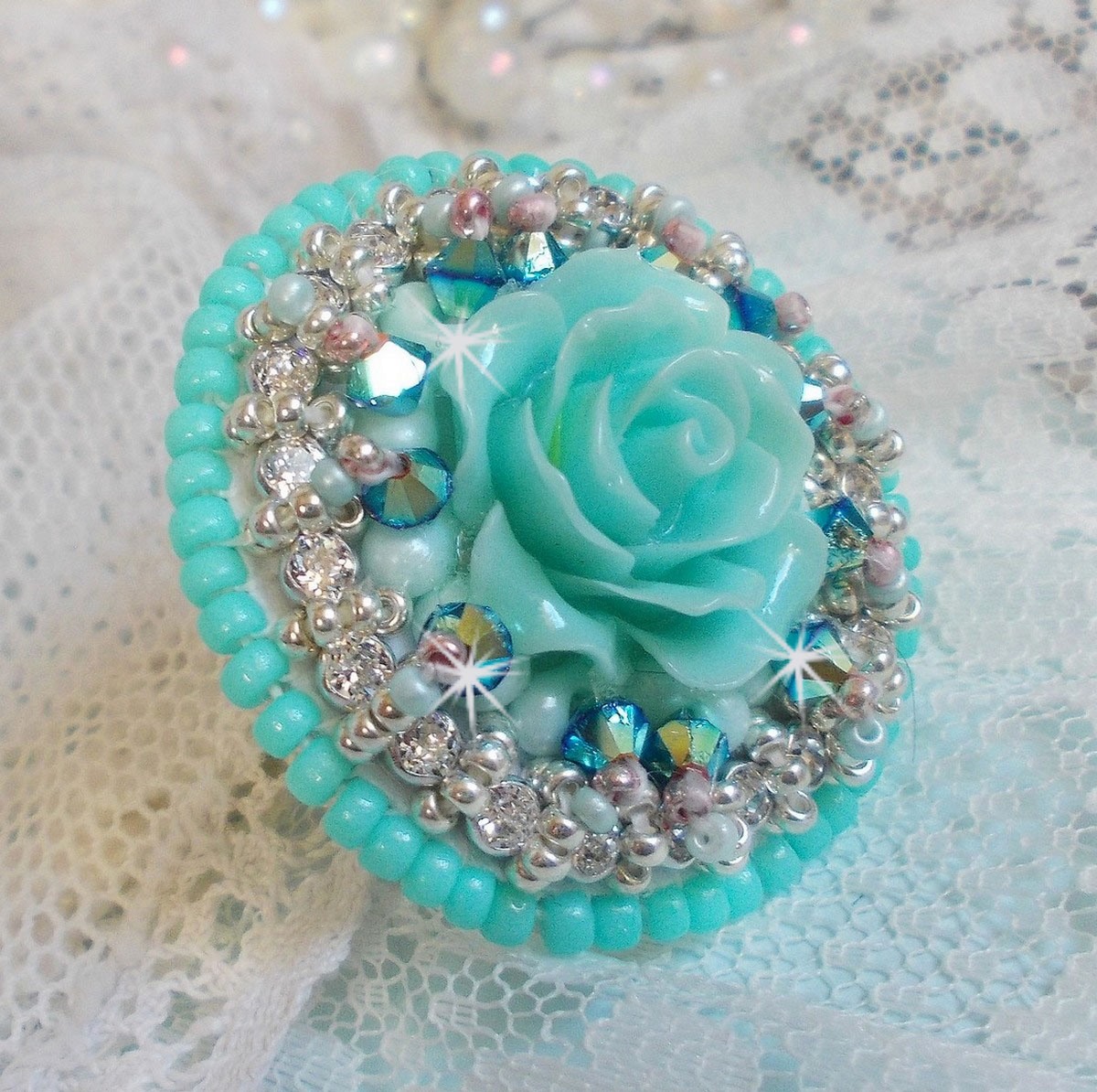 Bague Blue Flowers brod&eacute;e avec un cabochon en forme de rose en r&eacute;sine, cha&icirc;ne strass Cristal, toupies Jet de haute qualit&eacute; AB2X et farfalles ovales. Les couleurs sont : l&rsquo;Argent&eacute; et le Vert Menthe
