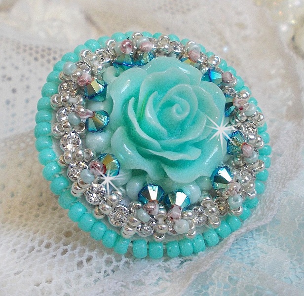 Bague Blue Flowers brod&eacute;e avec un cabochon en forme de rose en r&eacute;sine, cha&icirc;ne strass Cristal, toupies Jet de haute qualit&eacute; AB2X et farfalles ovales. Les couleurs sont : l&rsquo;Argent&eacute; et le Vert Menthe