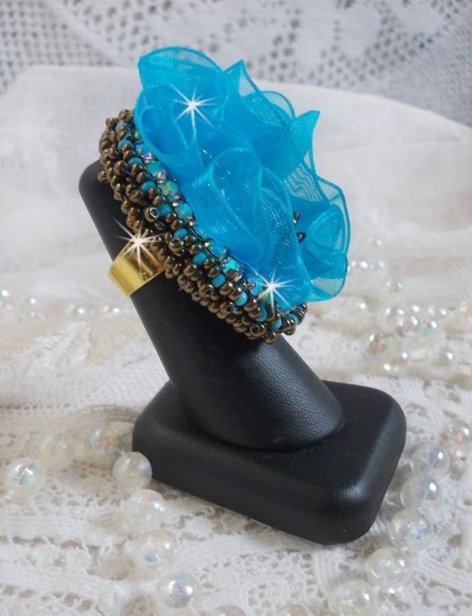 Bague artisanale brodée avec fleur bleue et perles dorées.