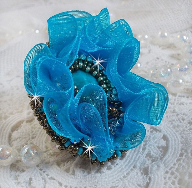 Bague artisanale bleue avec cabochon, perles et rubans ondulés.