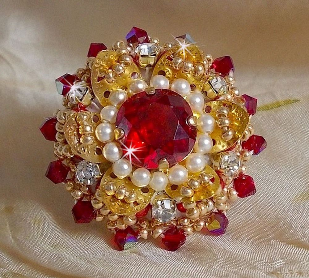 Bague L&rsquo;Oiseau des Iles Rouge Dor&eacute; avec un cabochon Rouge sur une estampe dor&eacute;e orn&eacute;e de cristaux : toupies et chatons. Les perles rondes nacr&eacute;es Ivoire et Rouge compl&egrave;tent cette bague r&eacute;glable Dor&eacute;e