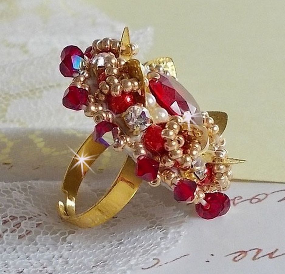 Bague L&rsquo;Oiseau des Iles Rouge Dor&eacute; avec un cabochon Rouge sur une estampe dor&eacute;e orn&eacute;e de cristaux : toupies et chatons. Les perles rondes nacr&eacute;es Ivoire et Rouge compl&egrave;tent cette bague r&eacute;glable Dor&eacute;e