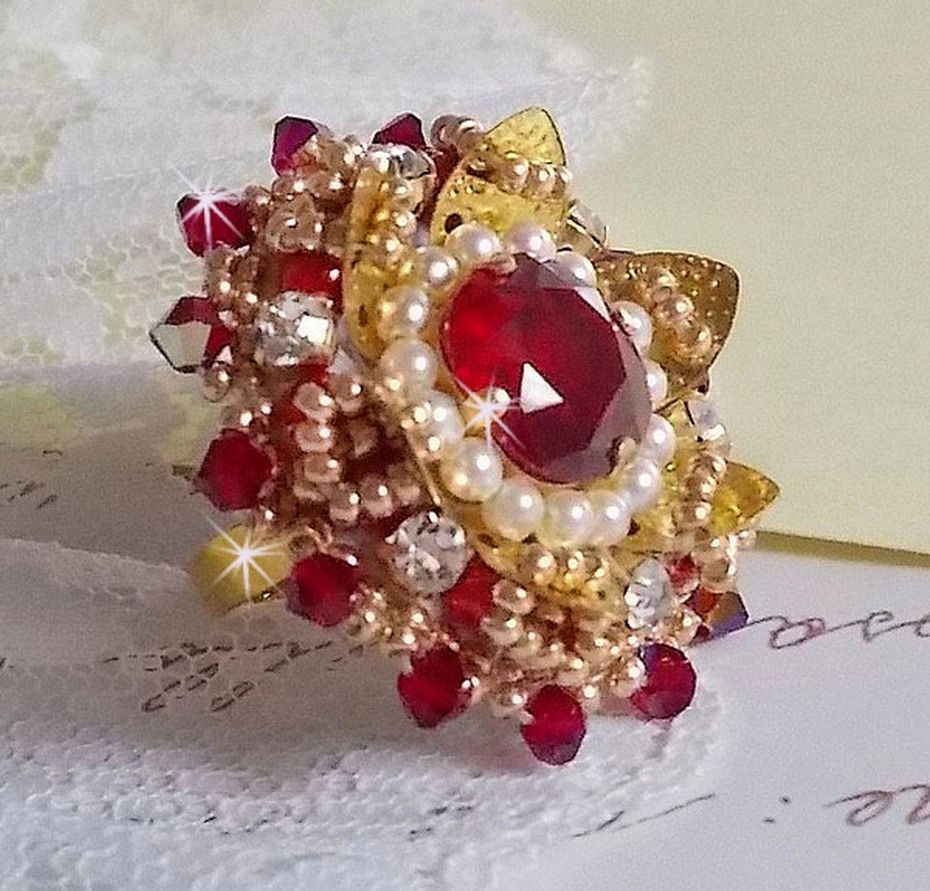 Bague L&rsquo;Oiseau des Iles Rouge Dor&eacute; avec un cabochon Rouge sur une estampe dor&eacute;e orn&eacute;e de cristaux : toupies et chatons. Les perles rondes nacr&eacute;es Ivoire et Rouge compl&egrave;tent cette bague r&eacute;glable Dor&eacute;e