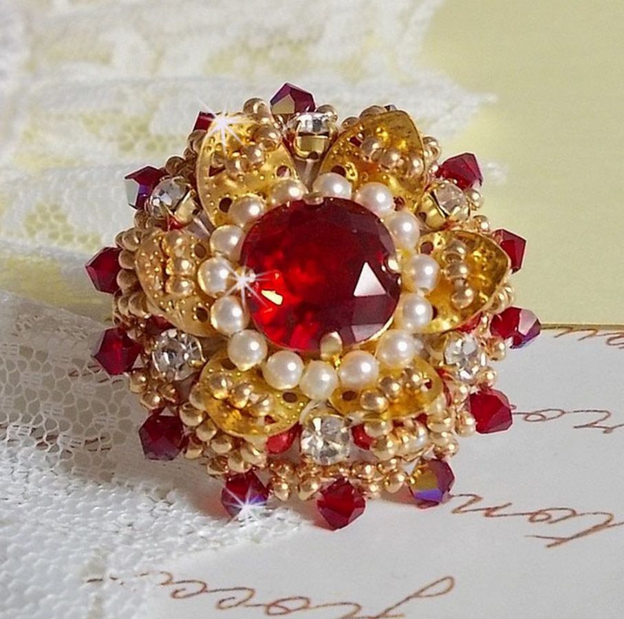 Bague L&rsquo;Oiseau des Iles Rouge Dor&eacute; avec un cabochon Rouge sur une estampe dor&eacute;e orn&eacute;e de cristaux : toupies et chatons. Les perles rondes nacr&eacute;es Ivoire et Rouge compl&egrave;tent cette bague r&eacute;glable Dor&eacute;e