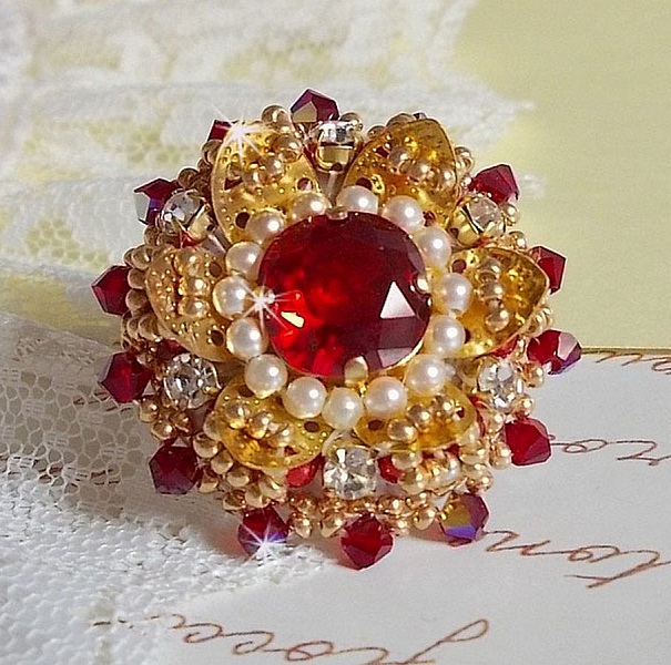 Bague L&rsquo;Oiseau des Iles Rouge Dor&eacute; avec un cabochon Rouge sur une estampe dor&eacute;e orn&eacute;e de cristaux : toupies et chatons. Les perles rondes nacr&eacute;es Ivoire et Rouge compl&egrave;tent cette bague r&eacute;glable Dor&eacute;e
