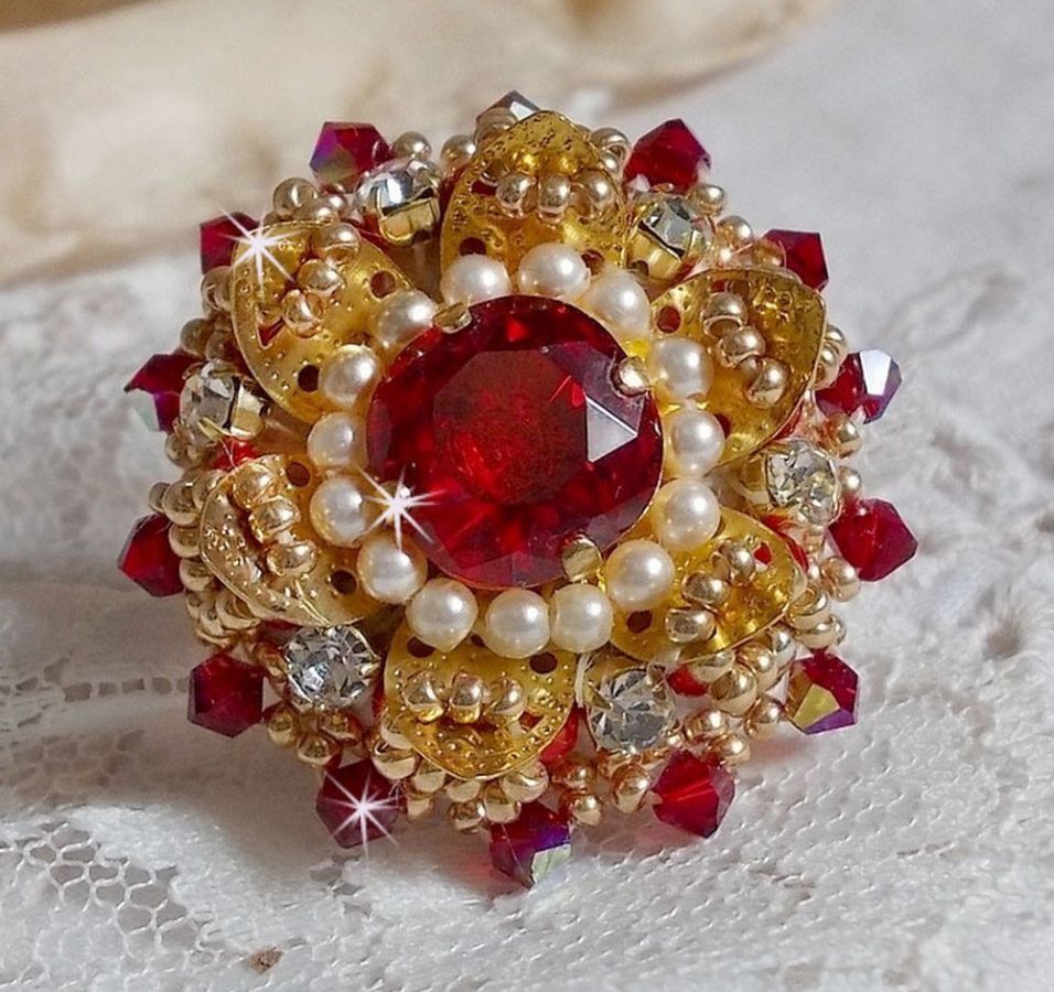 Bague L&rsquo;Oiseau des Iles Rouge Dor&eacute; avec un cabochon Rouge sur une estampe dor&eacute;e orn&eacute;e de cristaux : toupies et chatons. Les perles rondes nacr&eacute;es Ivoire et Rouge compl&egrave;tent cette bague r&eacute;glable Dor&eacute;e