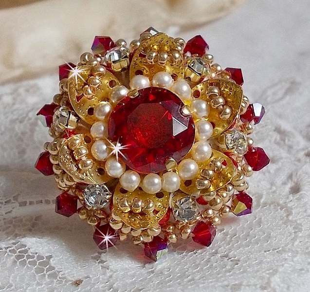 Bague L&rsquo;Oiseau des Iles Rouge Dor&eacute; avec un cabochon Rouge sur une estampe dor&eacute;e orn&eacute;e de cristaux : toupies et chatons. Les perles rondes nacr&eacute;es Ivoire et Rouge compl&egrave;tent cette bague r&eacute;glable Dor&eacute;e