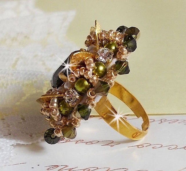 Bague L&rsquo;Oiseau des Iles Vert Dor&eacute;e avec un cabochon Vert sur une estampe dor&eacute;e orn&eacute;e de cristaux : toupies et chatons. Les perles rondes nacr&eacute;es Ivoire et Olivine compl&egrave;te cette bague r&eacute;glable. 