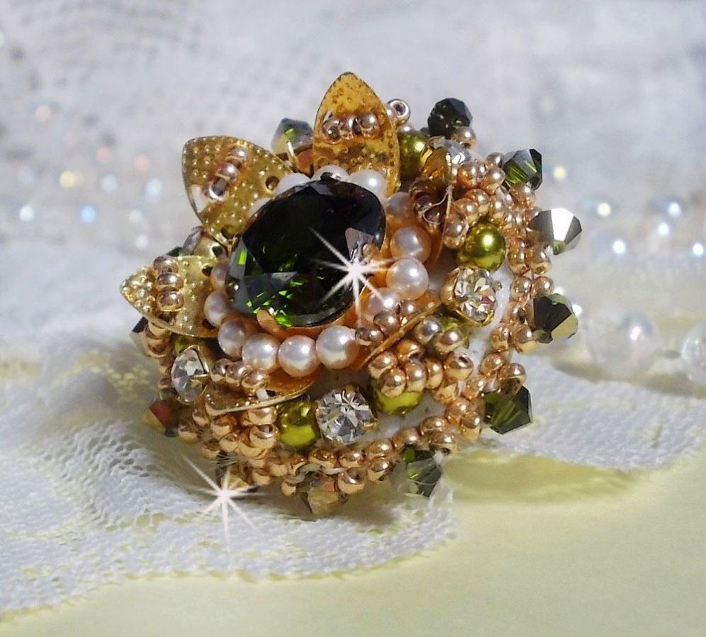 Bague L&rsquo;Oiseau des Iles Vert Dor&eacute;e avec un cabochon Vert sur une estampe dor&eacute;e orn&eacute;e de cristaux : toupies et chatons. Les perles rondes nacr&eacute;es Ivoire et Olivine compl&egrave;te cette bague r&eacute;glable. 