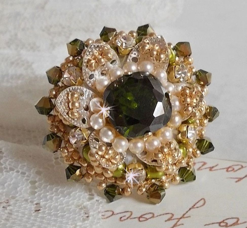 Bague L&rsquo;Oiseau des Iles Vert Argent avec un cabochon Vert sur une estampe Argent&eacute;e orn&eacute;e de cristaux : toupies et chatons. Les perles rondes nacr&eacute;es Ivoire et Olivine compl&egrave;te cette bague r&eacute;glable. 