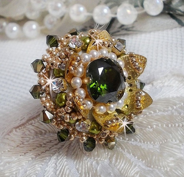 Bague L&rsquo;Oiseau des Iles Vert Dor&eacute;e avec un cabochon Vert sur une estampe dor&eacute;e orn&eacute;e de cristaux : toupies et chatons. Les perles rondes nacr&eacute;es Ivoire et Olivine compl&egrave;te cette bague r&eacute;glable. 