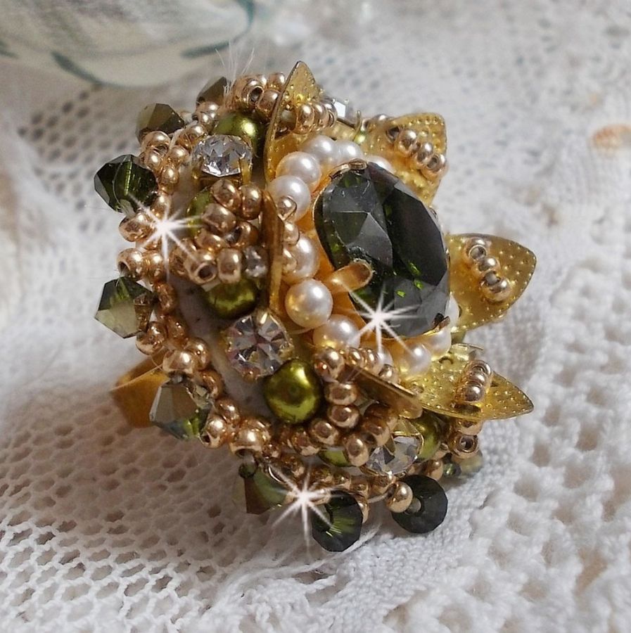 Bague L&rsquo;Oiseau des Iles Vert Dor&eacute;e avec un cabochon Vert sur une estampe dor&eacute;e orn&eacute;e de cristaux : toupies et chatons. Les perles rondes nacr&eacute;es Ivoire et Olivine compl&egrave;te cette bague r&eacute;glable. 