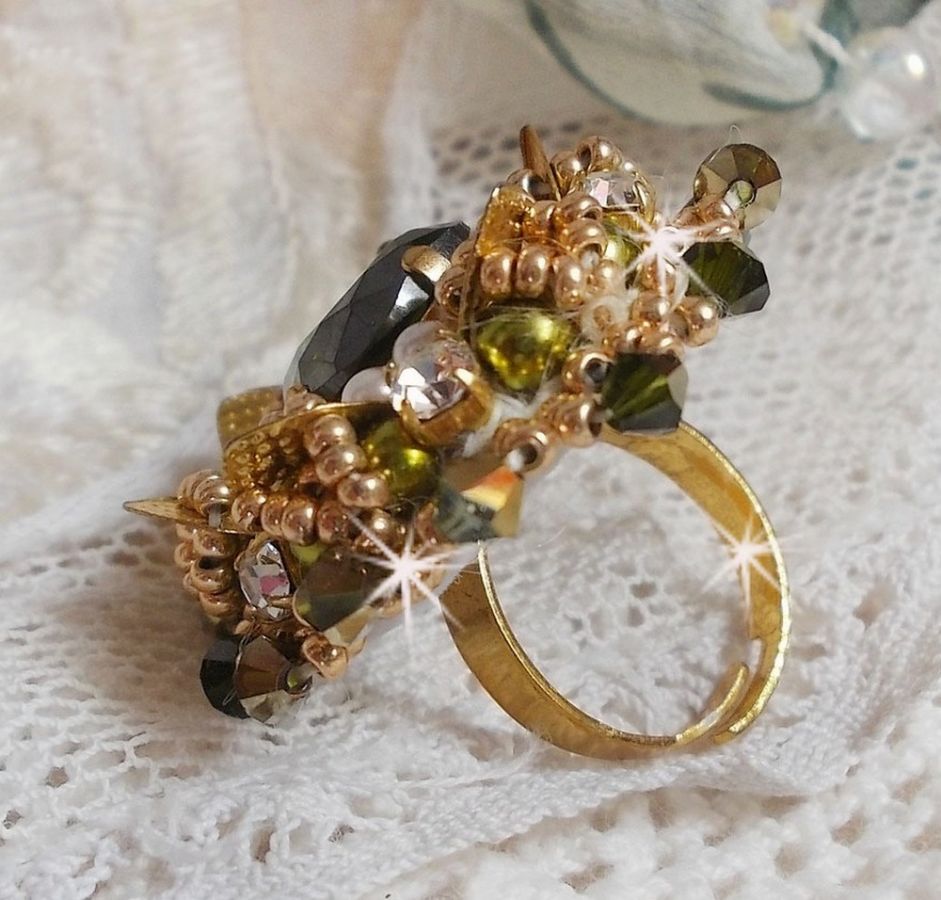 Bague L&rsquo;Oiseau des Iles Vert Dor&eacute;e avec un cabochon Vert sur une estampe dor&eacute;e orn&eacute;e de cristaux : toupies et chatons. Les perles rondes nacr&eacute;es Ivoire et Olivine compl&egrave;te cette bague r&eacute;glable. 