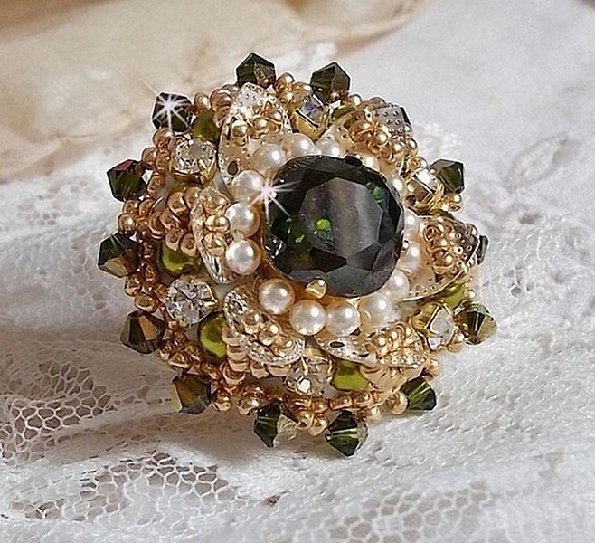 Bague L&rsquo;Oiseau des Iles Vert Argent avec un cabochon Vert sur une estampe Argent&eacute;e orn&eacute;e de cristaux : toupies et chatons. Les perles rondes nacr&eacute;es Ivoire et Olivine compl&egrave;te cette bague r&eacute;glable. 