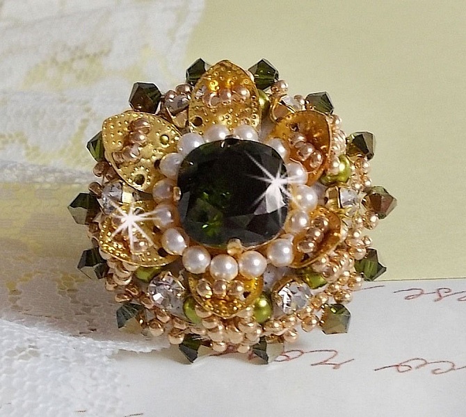 Bague L&rsquo;Oiseau des Iles Vert Dor&eacute;e avec un cabochon Vert sur une estampe dor&eacute;e orn&eacute;e de cristaux : toupies et chatons. Les perles rondes nacr&eacute;es Ivoire et Olivine compl&egrave;te cette bague r&eacute;glable. 