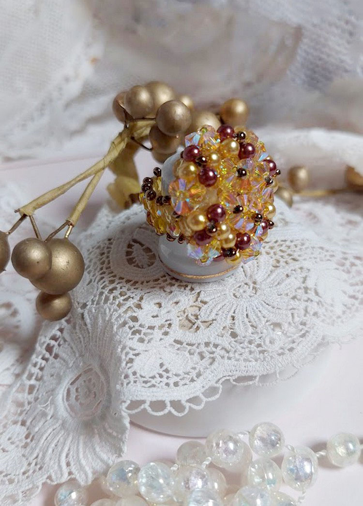 Bague Soleil mont&eacute;e avec des toupies en Cristal de Swarovski aux couleurs Topaze, Gold et Marron &agrave; laquelle s&rsquo;ajoute des facettes en Verre de Boh&egrave;me. Les perles s&rsquo;entrelacent avec les rocailles Dor&eacute;es