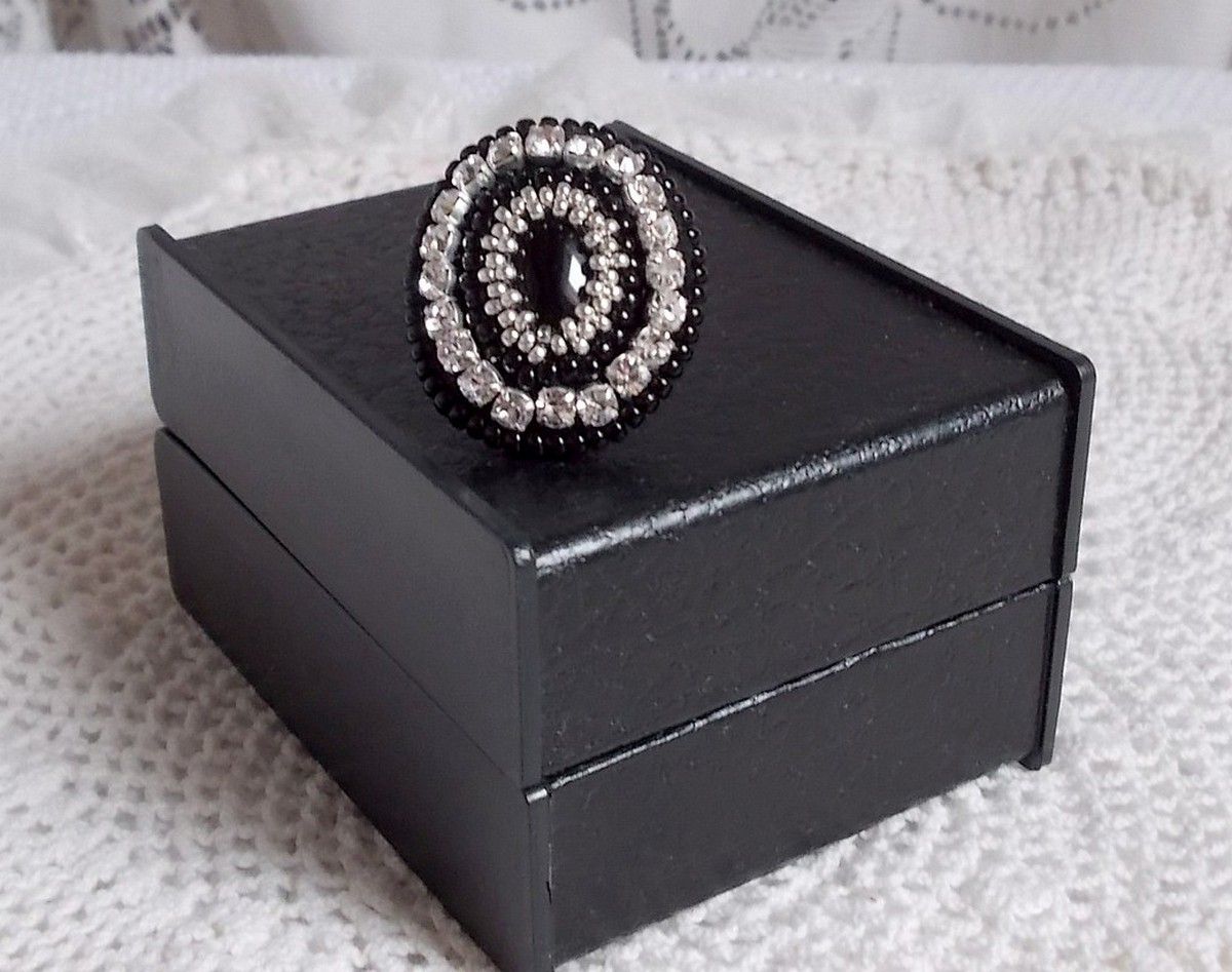 Bague Stone Noire avec un cabochon en Onyx orn&eacute; de chatons en Cristal &agrave; laquelle s&rsquo;ajoute des rocailles Argent&eacute;es qui compl&egrave;tent le Noir sur bague Nickel en Laiton et une feutrine. Un style R&eacute;tro