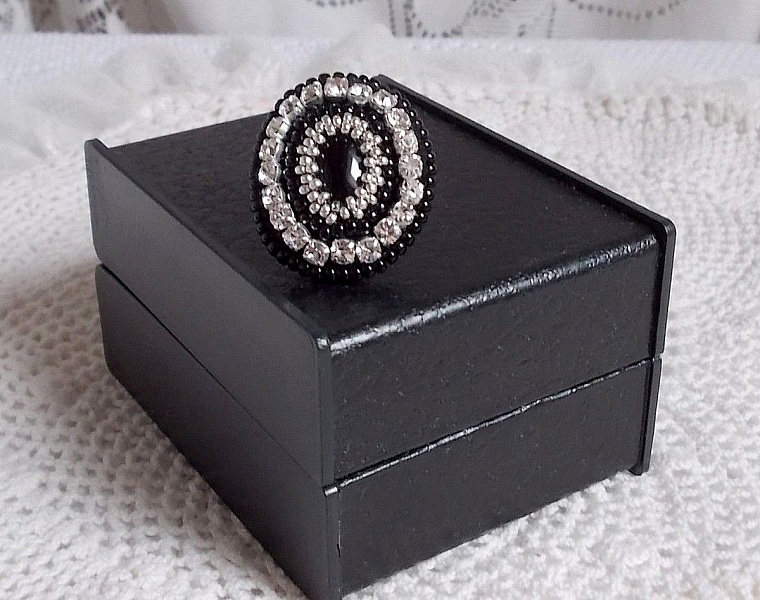 Bague Stone Noire avec un cabochon en Onyx orn&eacute; de chatons en Cristal &agrave; laquelle s&rsquo;ajoute des rocailles Argent&eacute;es qui compl&egrave;tent le Noir sur bague Nickel en Laiton et une feutrine. Un style R&eacute;tro