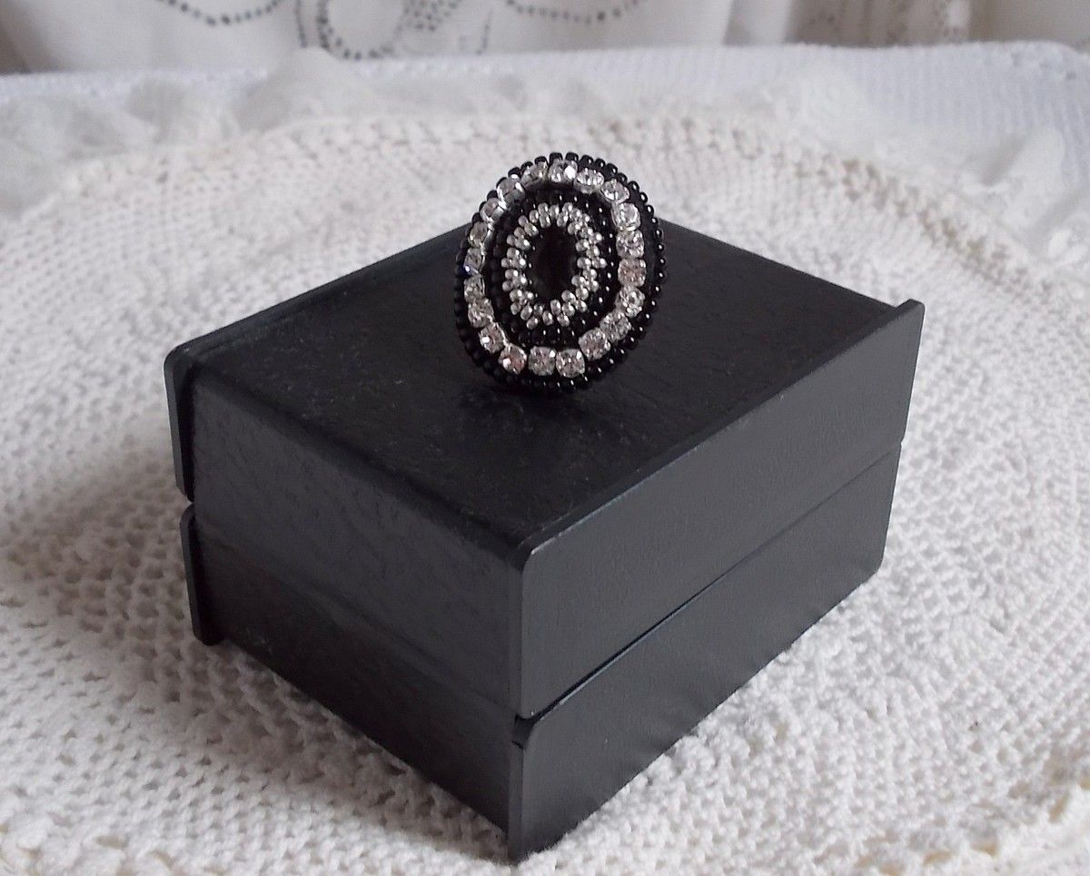 Bague Stone Noire avec un cabochon en Onyx orn&eacute; de chatons en Cristal &agrave; laquelle s&rsquo;ajoute des rocailles Argent&eacute;es qui compl&egrave;tent le Noir sur bague Nickel en Laiton et une feutrine. Un style R&eacute;tro
