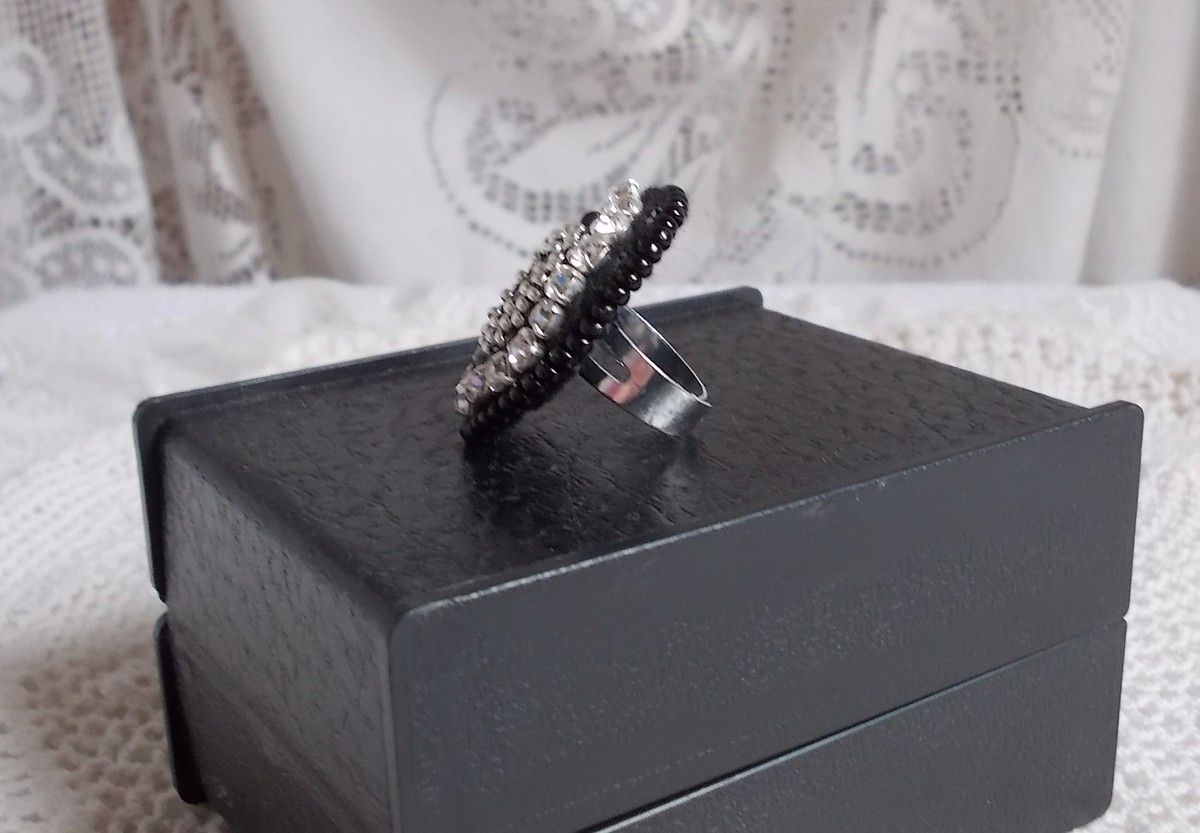 Bague Stone Noire avec un cabochon en Onyx orn&eacute; de chatons en Cristal &agrave; laquelle s&rsquo;ajoute des rocailles Argent&eacute;es qui compl&egrave;tent le Noir sur bague Nickel en Laiton et une feutrine. Un style R&eacute;tro