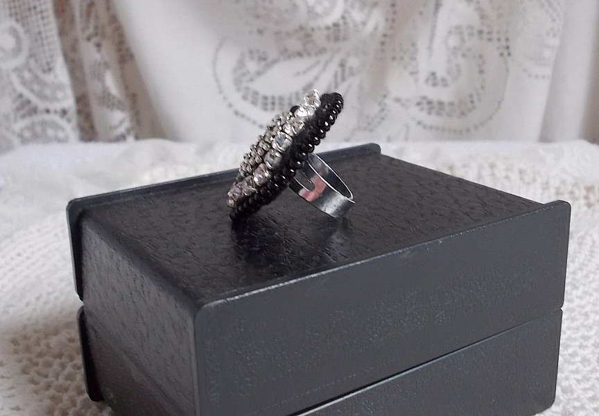 Bague Stone Noire avec un cabochon en Onyx orn&eacute; de chatons en Cristal &agrave; laquelle s&rsquo;ajoute des rocailles Argent&eacute;es qui compl&egrave;tent le Noir sur bague Nickel en Laiton et une feutrine. Un style R&eacute;tro