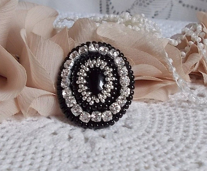 Bague Stone Noire avec un cabochon en Onyx orn&eacute; de chatons en Cristal &agrave; laquelle s&rsquo;ajoute des rocailles Argent&eacute;es qui compl&egrave;tent le Noir sur bague Nickel en Laiton et une feutrine. Un style R&eacute;tro