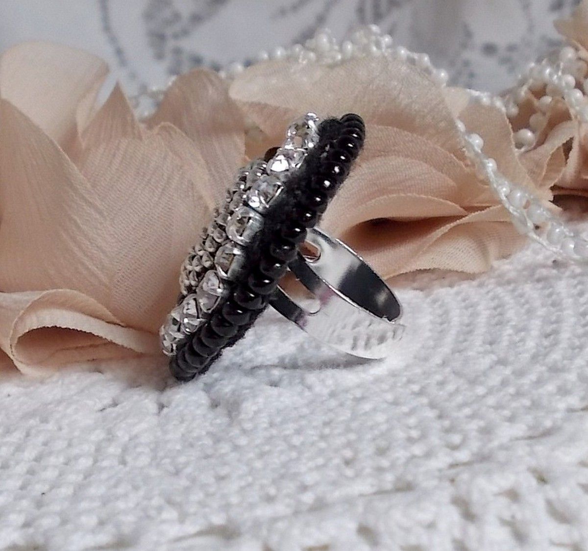 Bague Stone Noire avec un cabochon en Onyx orn&eacute; de chatons en Cristal &agrave; laquelle s&rsquo;ajoute des rocailles Argent&eacute;es qui compl&egrave;tent le Noir sur bague Nickel en Laiton et une feutrine. Un style R&eacute;tro