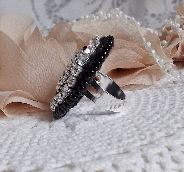 Bague Stone Noire avec un cabochon en Onyx orn&eacute; de chatons en Cristal &agrave; laquelle s&rsquo;ajoute des rocailles Argent&eacute;es qui compl&egrave;tent le Noir sur bague Nickel en Laiton et une feutrine. Un style R&eacute;tro