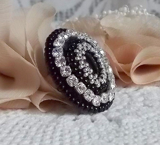 Bague Stone Noire avec un cabochon en Onyx orn&eacute; de chatons en Cristal &agrave; laquelle s&rsquo;ajoute des rocailles Argent&eacute;es qui compl&egrave;tent le Noir sur bague Nickel en Laiton et une feutrine. Un style R&eacute;tro