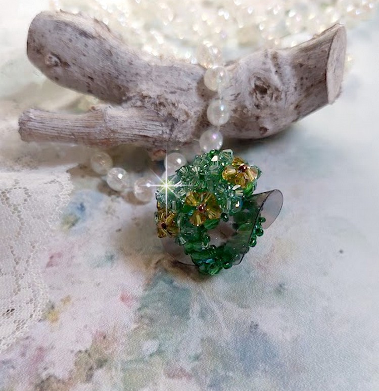 Bague Vert Tendre mont&eacute;e avec des toupies en Cristal dans les nuances de Vert Emerald et Jaune &agrave; laquelle s'ajoute des facettes et des rocailles. Un feuillage verdoyant de fleurs