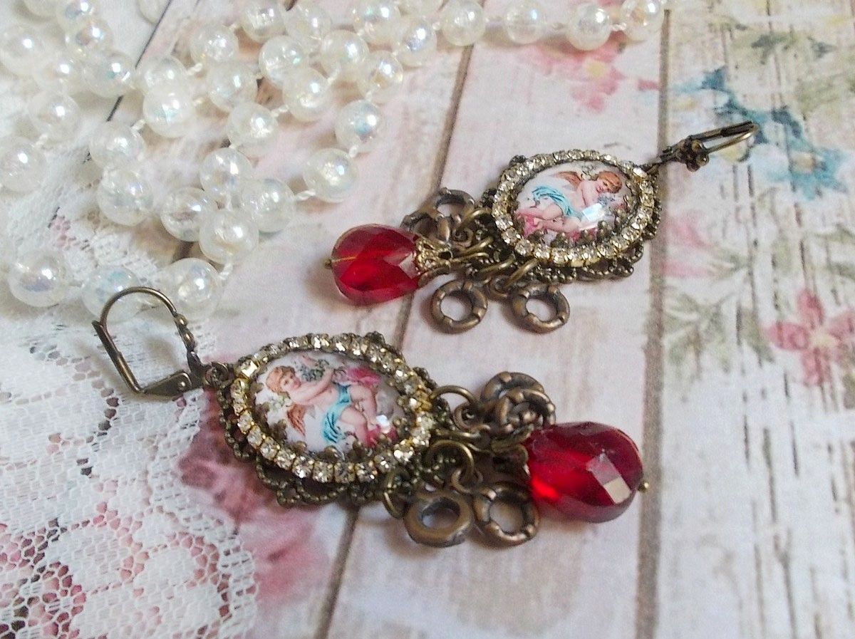 BO Petit Ange avec des cabochons d&rsquo;anges orn&eacute;s d&rsquo;une cha&icirc;ne strass Cristal, breloques, gouttes facett&eacute;es en verre de couleur Siam. Mont&eacute;s sur des pendentifs et des dormeuses en Laiton