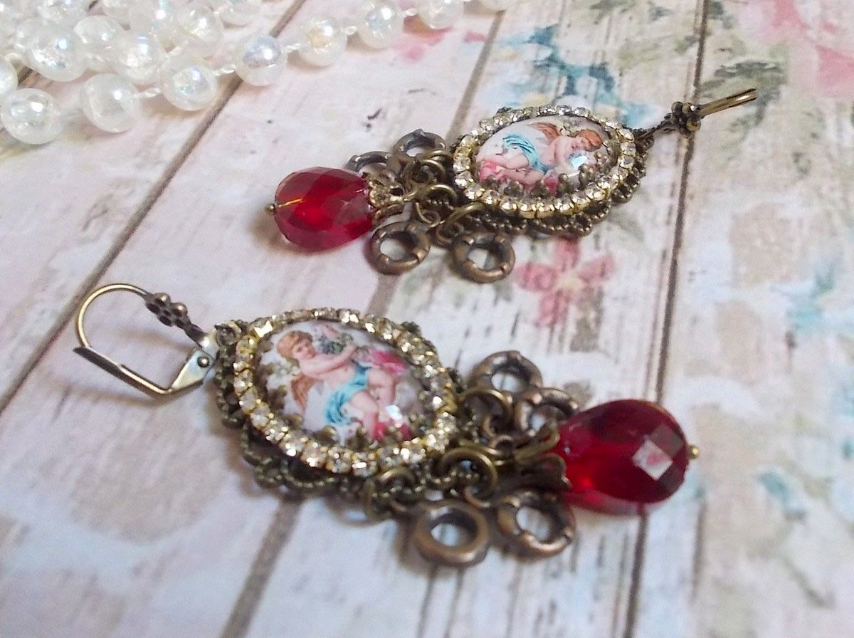 BO Petit Ange avec des cabochons d&rsquo;anges orn&eacute;s d&rsquo;une cha&icirc;ne strass Cristal, breloques, gouttes facett&eacute;es en verre de couleur Siam. Mont&eacute;s sur des pendentifs et des dormeuses en Laiton