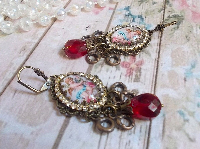 BO Petit Ange avec des cabochons d&rsquo;anges orn&eacute;s d&rsquo;une cha&icirc;ne strass Cristal, breloques, gouttes facett&eacute;es en verre de couleur Siam. Mont&eacute;s sur des pendentifs et des dormeuses en Laiton