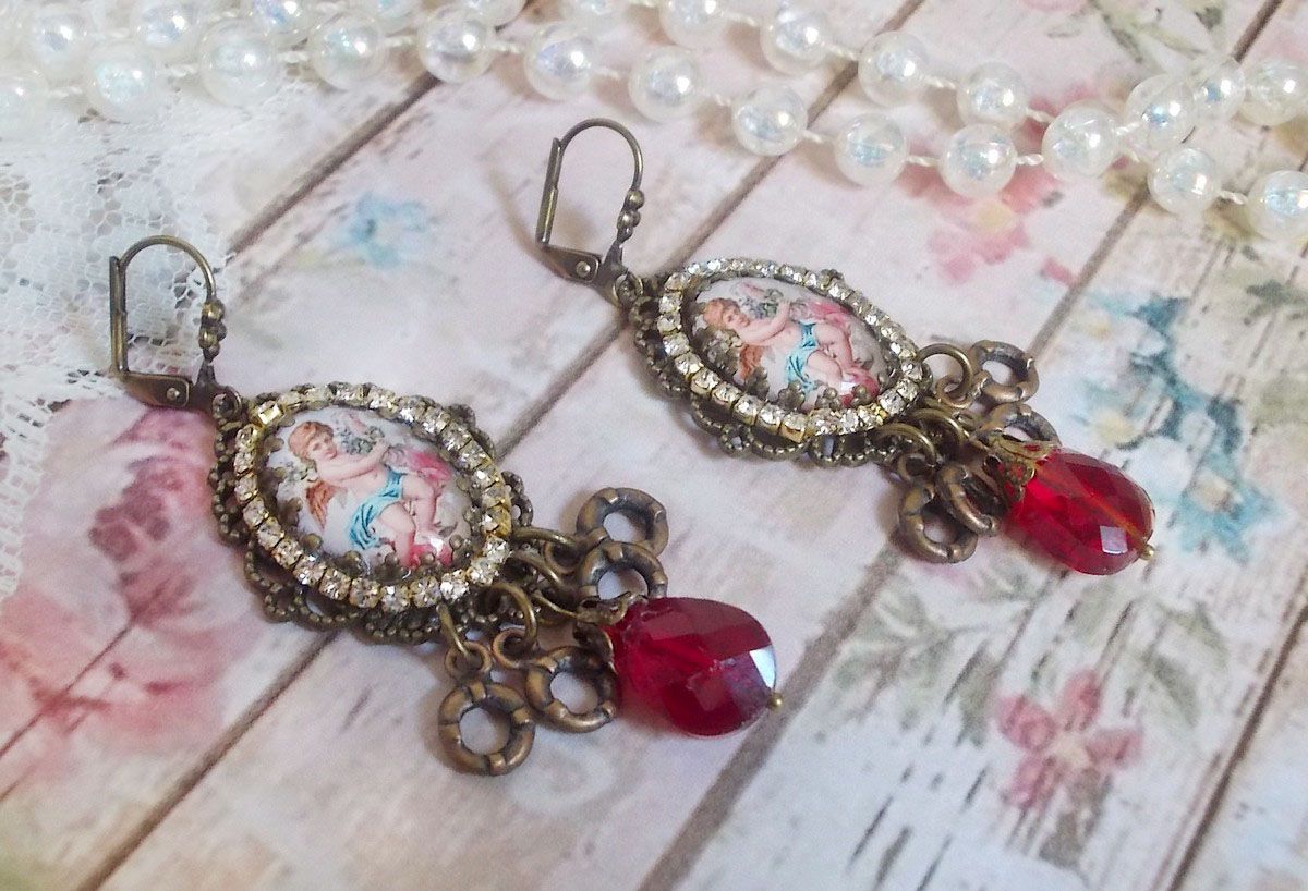 BO Petit Ange avec des cabochons d&rsquo;anges orn&eacute;s d&rsquo;une cha&icirc;ne strass Cristal, breloques, gouttes facett&eacute;es en verre de couleur Siam. Mont&eacute;s sur des pendentifs et des dormeuses en Laiton