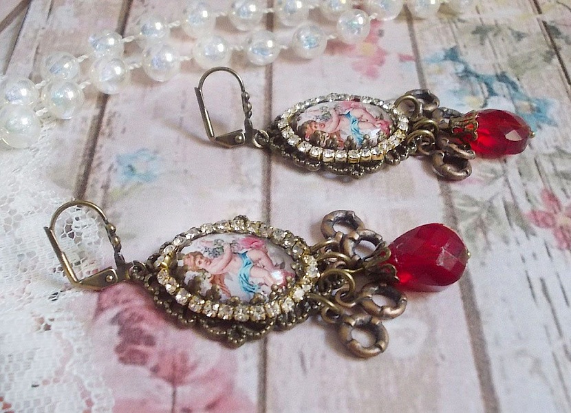 BO Petit Ange avec des cabochons d&rsquo;anges orn&eacute;s d&rsquo;une cha&icirc;ne strass Cristal, breloques, gouttes facett&eacute;es en verre de couleur Siam. Mont&eacute;s sur des pendentifs et des dormeuses en Laiton