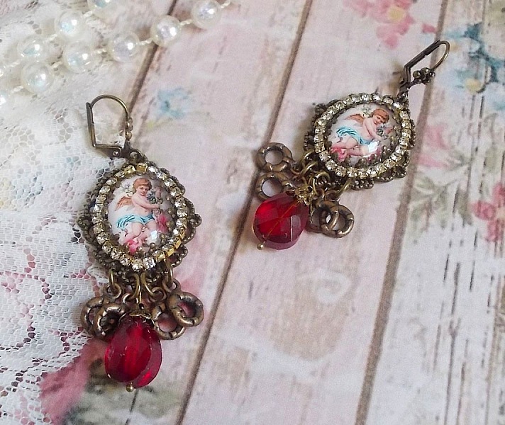 BO Petit Ange avec des cabochons d&rsquo;anges orn&eacute;s d&rsquo;une cha&icirc;ne strass Cristal, breloques, gouttes facett&eacute;es en verre de couleur Siam. Mont&eacute;s sur des pendentifs et des dormeuses en Laiton