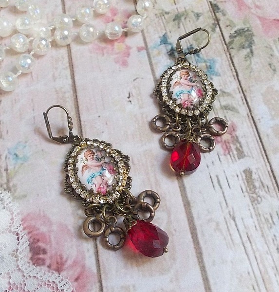 BO Petit Ange avec des cabochons d&rsquo;anges orn&eacute;s d&rsquo;une cha&icirc;ne strass Cristal, breloques, gouttes facett&eacute;es en verre de couleur Siam. Mont&eacute;s sur des pendentifs et des dormeuses en Laiton