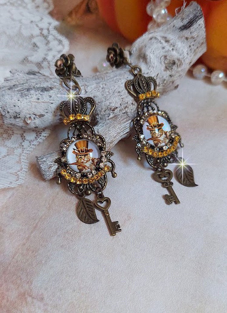 BO Chatibo Steampunk mont&eacute;es avec cabochons ronds en verre repr&eacute;sentant un chat chapeaut&eacute; Haute de Forme Orange. Strass&eacute;es avec une couronne, breloques cl&eacute;s et feuilles. Mont&eacute;es sur clips Bronze