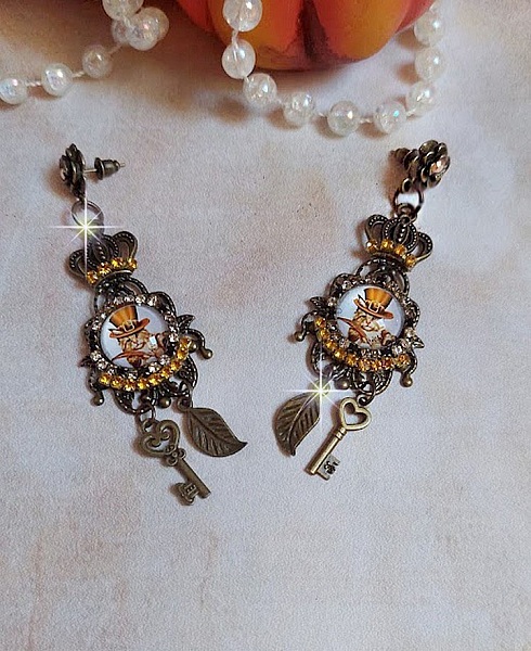BO Chatibo Steampunk mont&eacute;es avec cabochons ronds en verre repr&eacute;sentant un chat chapeaut&eacute; Haute de Forme Orange. Strass&eacute;es avec une couronne, breloques cl&eacute;s et feuilles. Mont&eacute;es sur clips Bronze