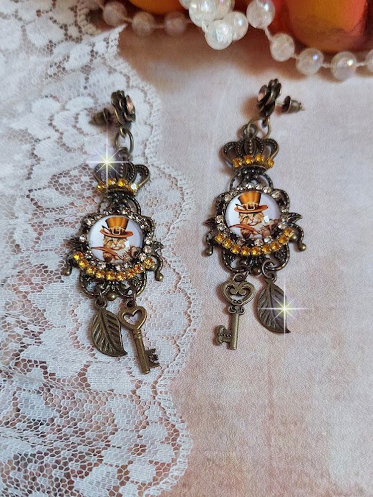 BO Chatibo Steampunk mont&eacute;es avec cabochons ronds en verre repr&eacute;sentant un chat chapeaut&eacute; Haute de Forme Orange. Strass&eacute;es avec une couronne, breloques cl&eacute;s et feuilles. Mont&eacute;es sur clips Bronze