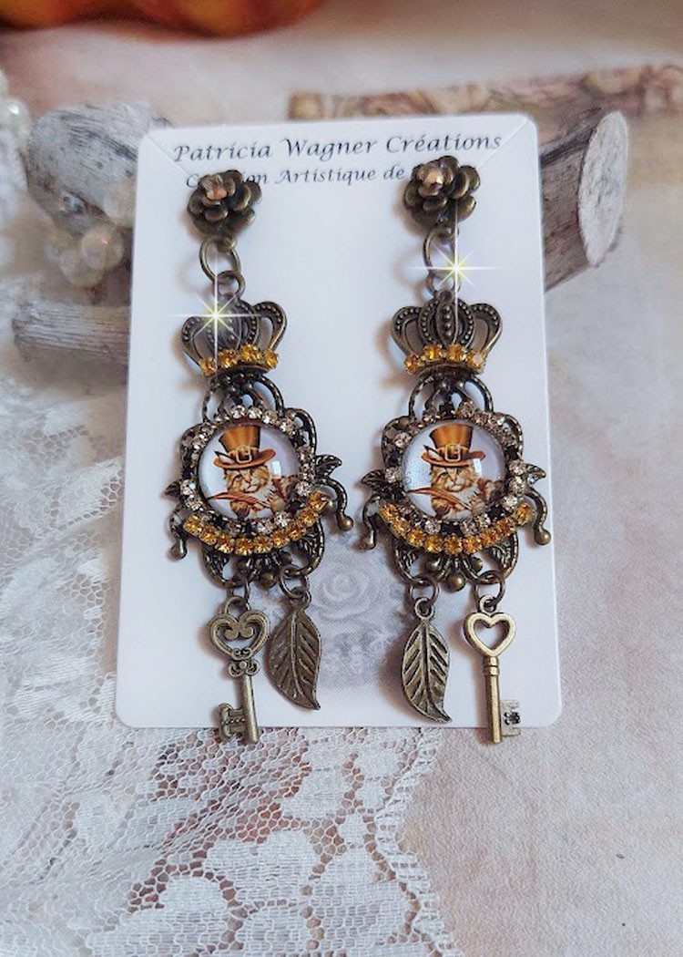 BO Chatibo Steampunk mont&eacute;es avec cabochons ronds en verre repr&eacute;sentant un chat chapeaut&eacute; Haute de Forme Orange. Strass&eacute;es avec une couronne, breloques cl&eacute;s et feuilles. Mont&eacute;es sur clips Bronze