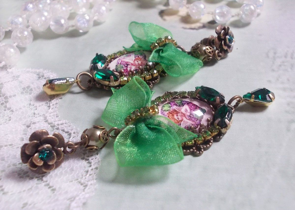BO C&oelig;ur d&rsquo;Anges avec des cabochons d&rsquo;un petit ange orn&eacute;s d&rsquo;une cha&icirc;ne strass, navettes, poires et cabochons en Cristal. S&rsquo;ajoute des rubans organza sur pendentifs et clous en forme de fleurs.