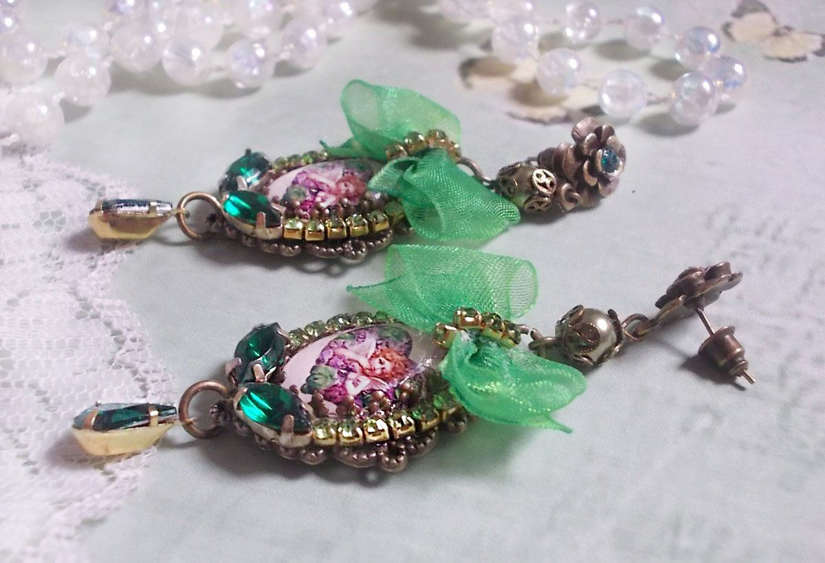 BO C&oelig;ur d&rsquo;Anges avec des cabochons d&rsquo;un petit ange orn&eacute;s d&rsquo;une cha&icirc;ne strass, navettes, poires et cabochons en Cristal. S&rsquo;ajoute des rubans organza sur pendentifs et clous en forme de fleurs.