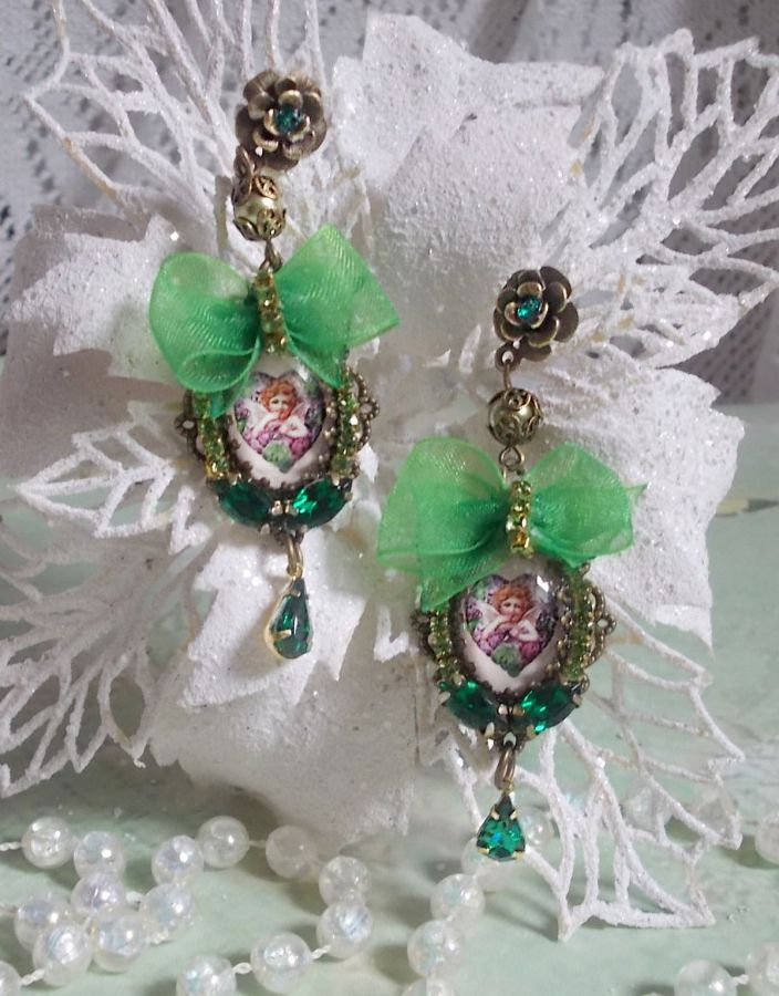 BO C&oelig;ur d&rsquo;Anges avec des cabochons d&rsquo;un petit ange orn&eacute;s d&rsquo;une cha&icirc;ne strass, navettes, poires et cabochons en Cristal. S&rsquo;ajoute des rubans organza sur pendentifs et clous en forme de fleurs.