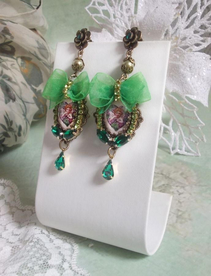 BO C&oelig;ur d&rsquo;Anges avec des cabochons d&rsquo;un petit ange orn&eacute;s d&rsquo;une cha&icirc;ne strass, navettes, poires et cabochons en Cristal. S&rsquo;ajoute des rubans organza sur pendentifs et clous en forme de fleurs.